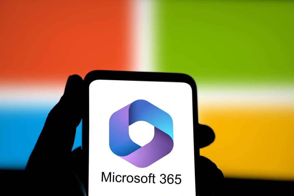 A person holds a smartphone showing the Microsoft 365 logo, with the colorful Microsoft logo in the background, highlighting Microsoft 365 Backup and IT Services.