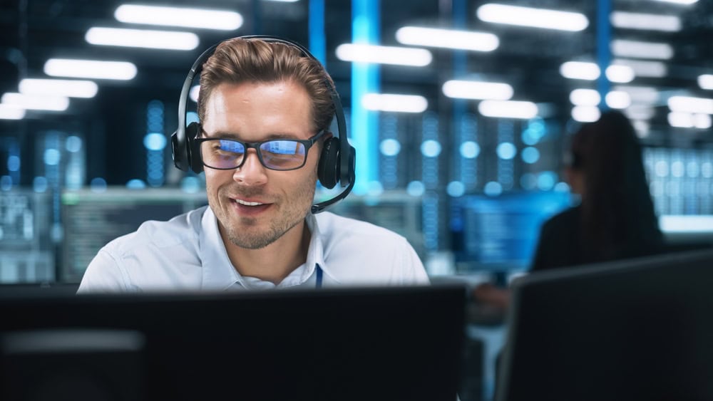 A man with glasses and a headset smiles while managing cybersecurity tasks on his computer, providing IT support in Indiana and Illinois.