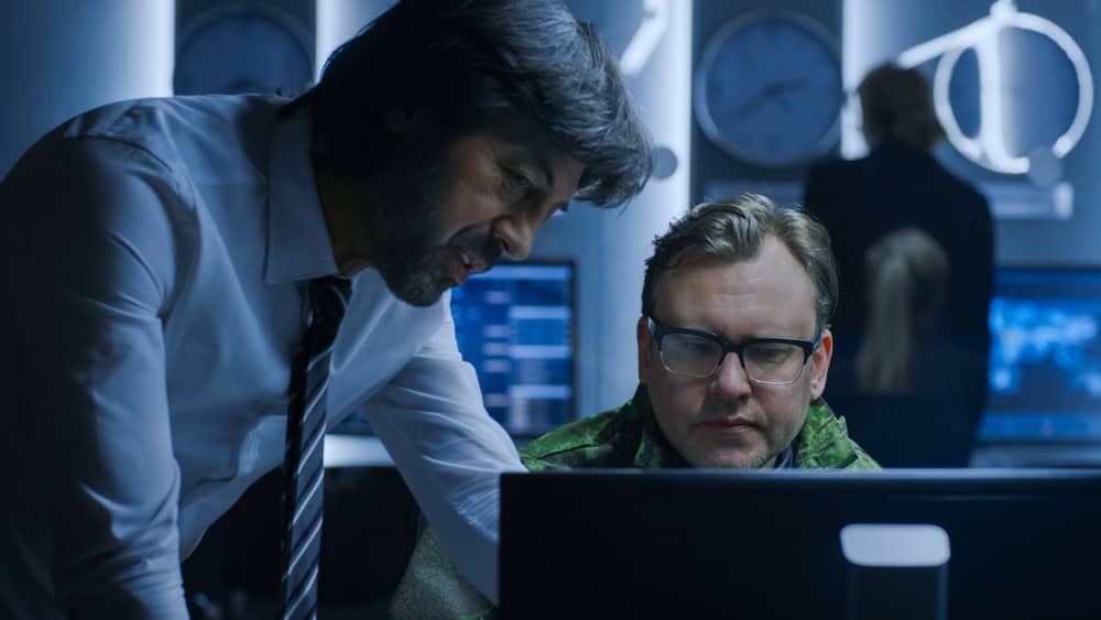 Two men analyze a computer in a dim IT room in Danville, surrounded by digital gear—offering Managed IT & Cybersecurity Services in IL & IN.