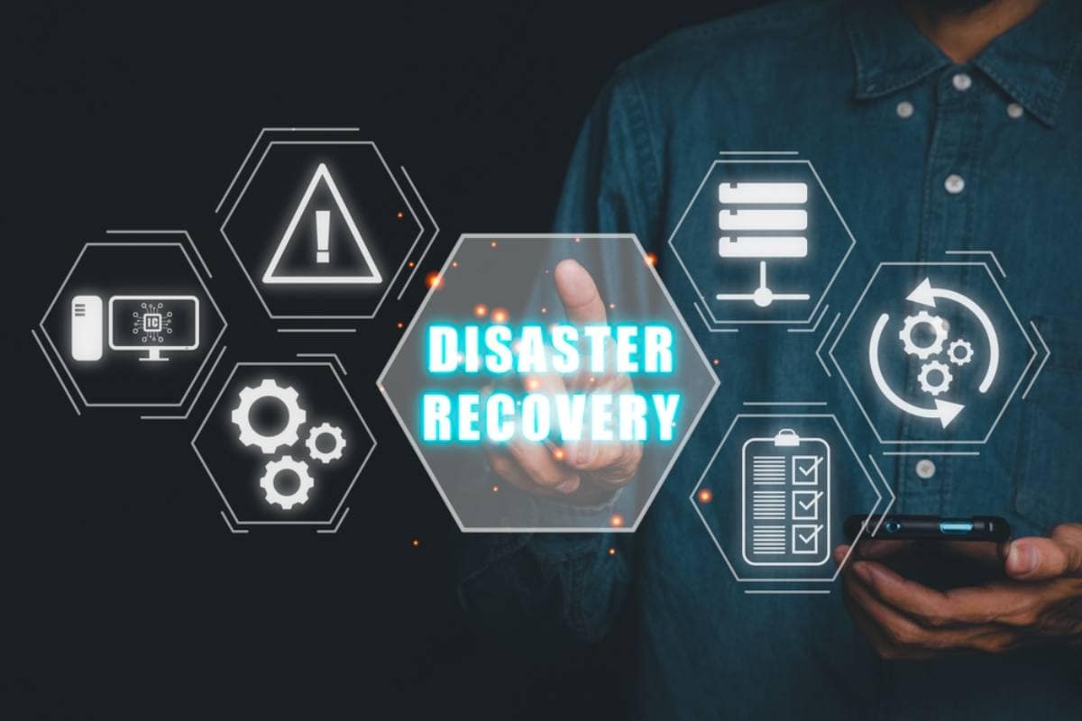 A person in a denim shirt touches a virtual screen displaying the words "DISASTER RECOVERY" surrounded by digital icons, including gears, warning signs, checklists, and circular arrows.