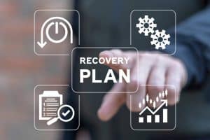 A person points to a transparent virtual screen displaying icons for process, checklist, gears, and bar graph, with “RECOVERY PLAN” highlighted in the center. The background is blurred.