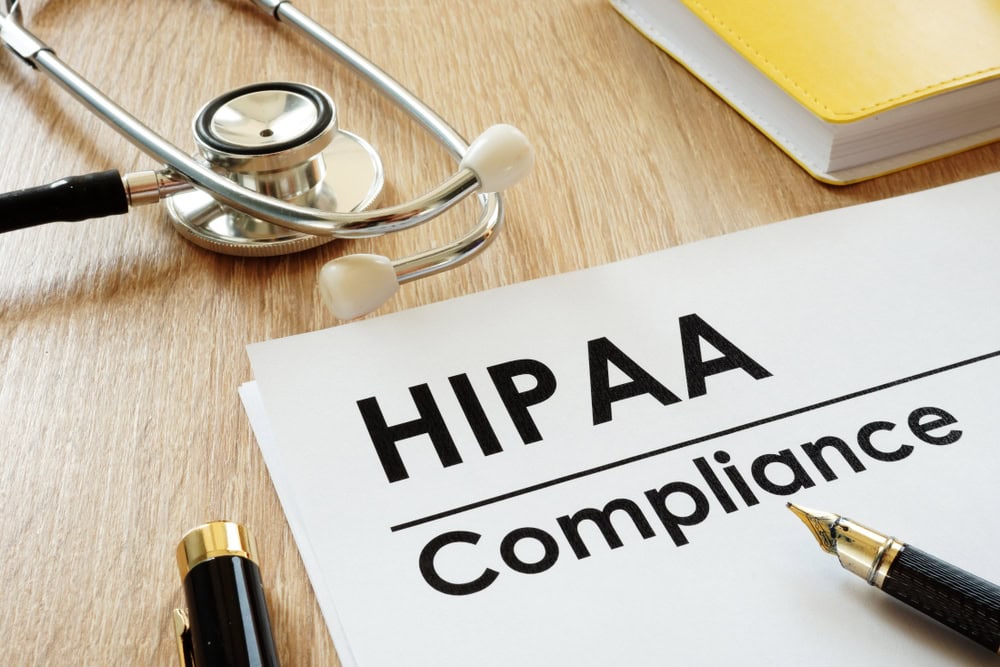 A document labeled "HIPAA Compliance" on a desk, with a stethoscope, pen, and yellow notebook nearby, representing healthcare privacy regulations.
