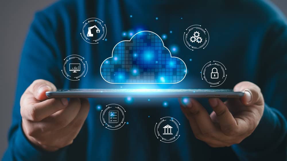 A person holds a tablet with a glowing digital cloud icon above it, surrounded by technology, security, banking, and automation icons, representing cloud computing and digital data integration.